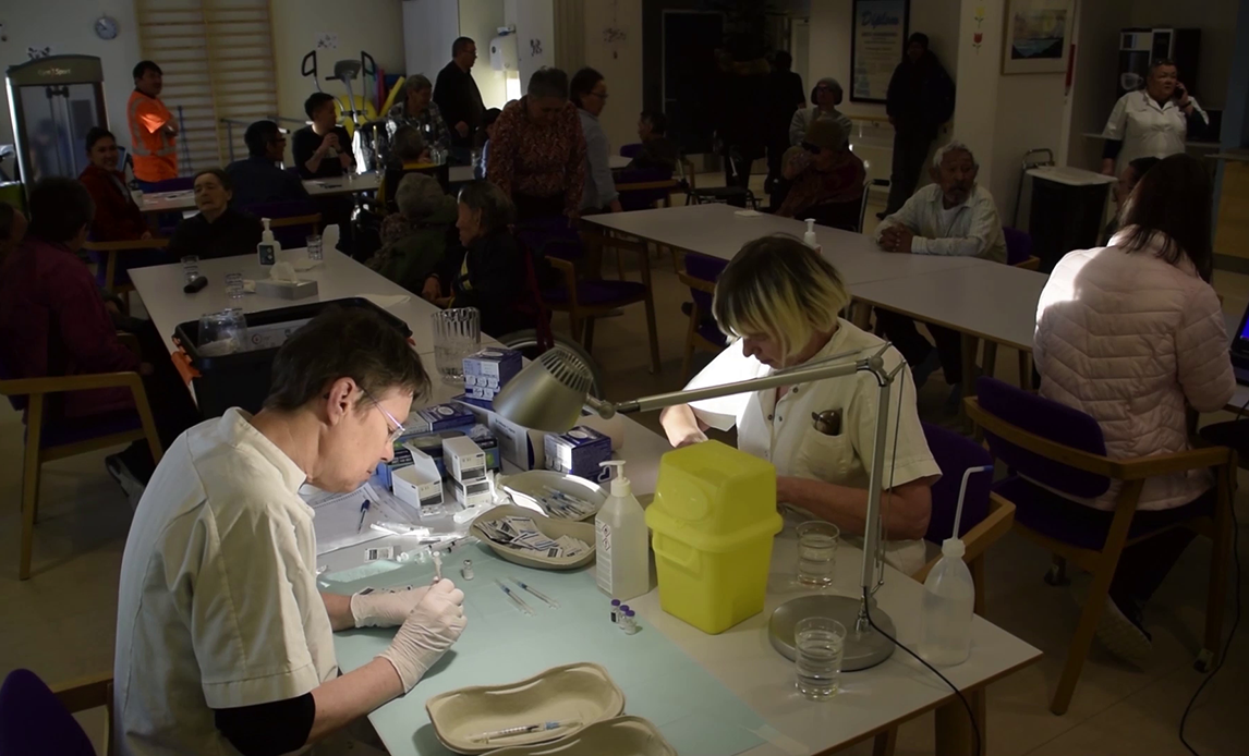 To sundhedspersonel klargør vacciner i rum med ventende borgere i Paamiut, Grønland.